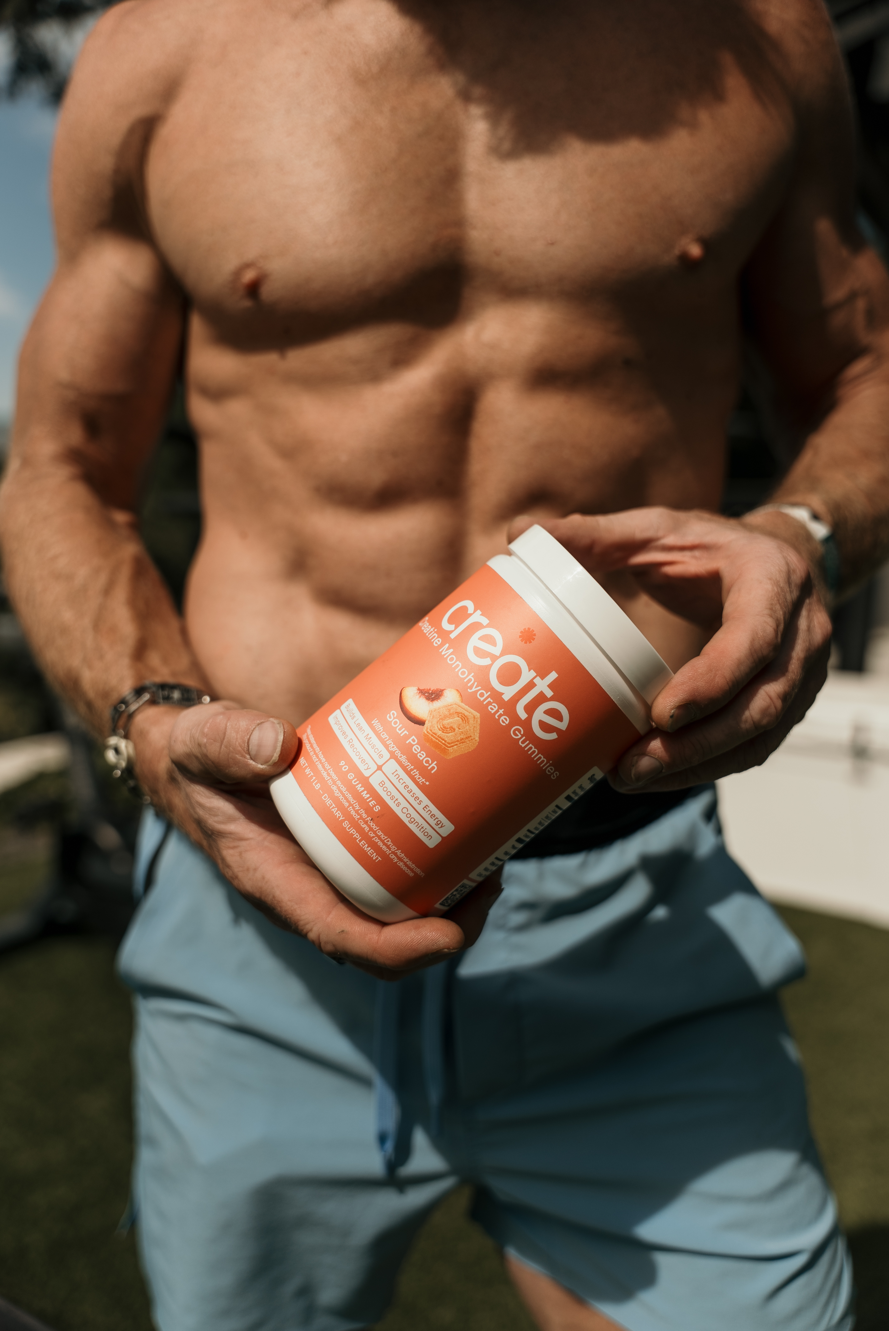 Person holding a container of creatine gummies outdoors.