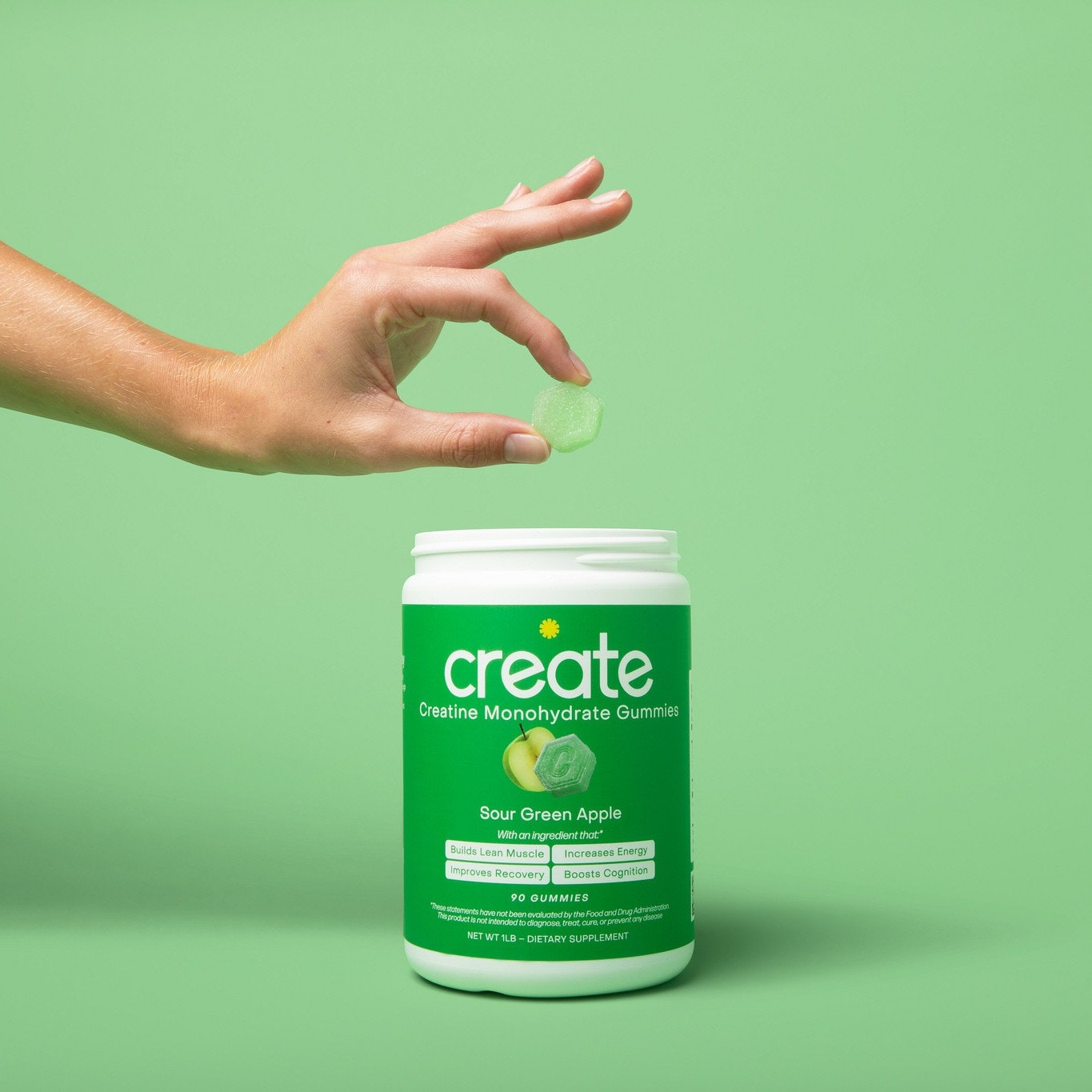 Hand holding a gummy above a green container on a matching background.