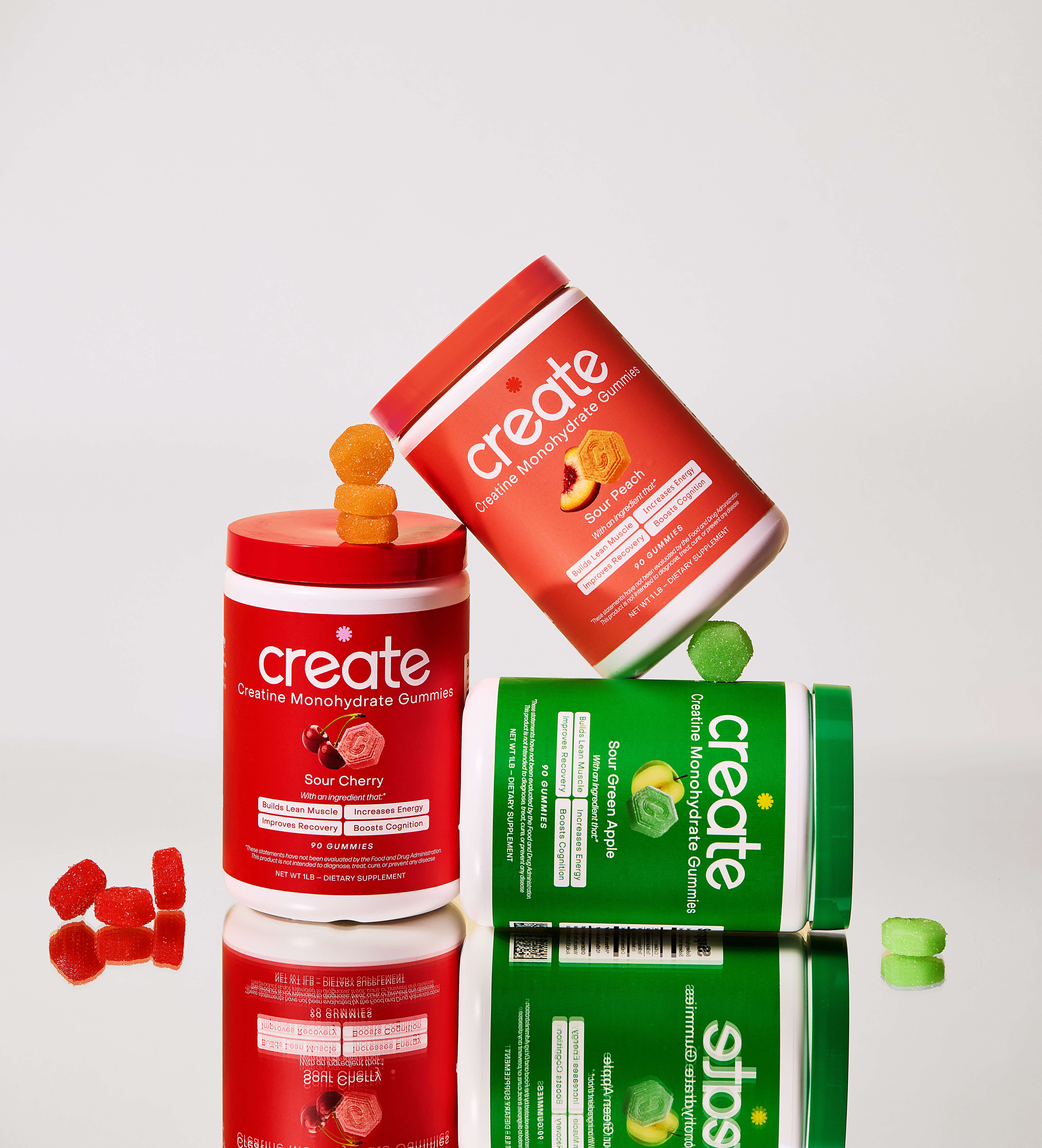 Three jars of creatine monohydrate gummies in red and green, with gummy pieces scattered.