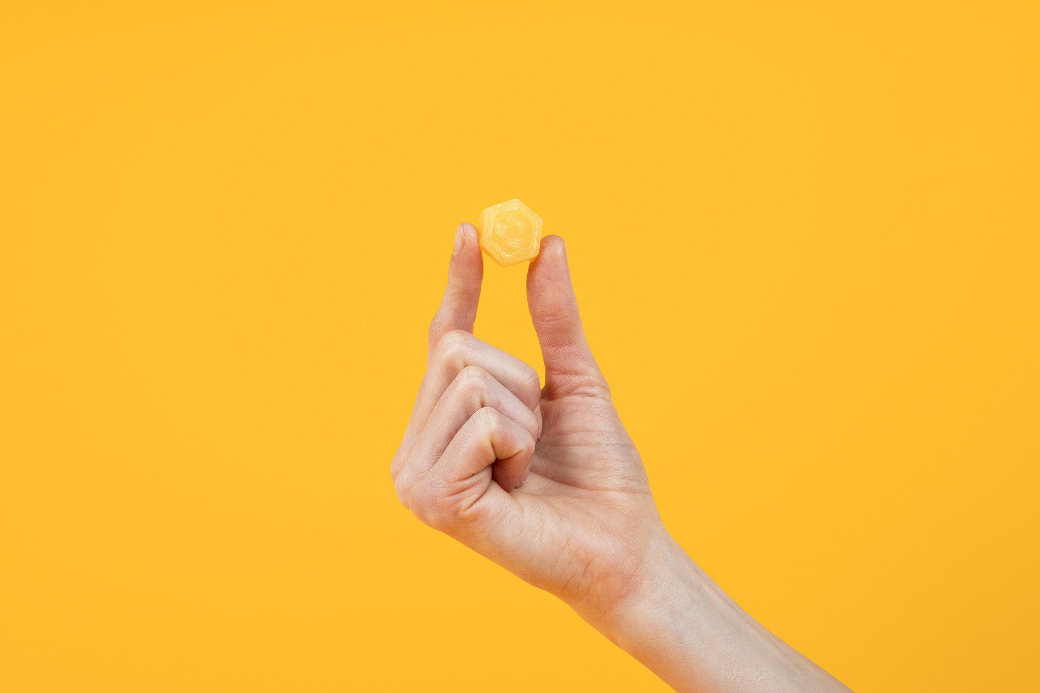 Hand holding a small hexagonal object against a yellow background.