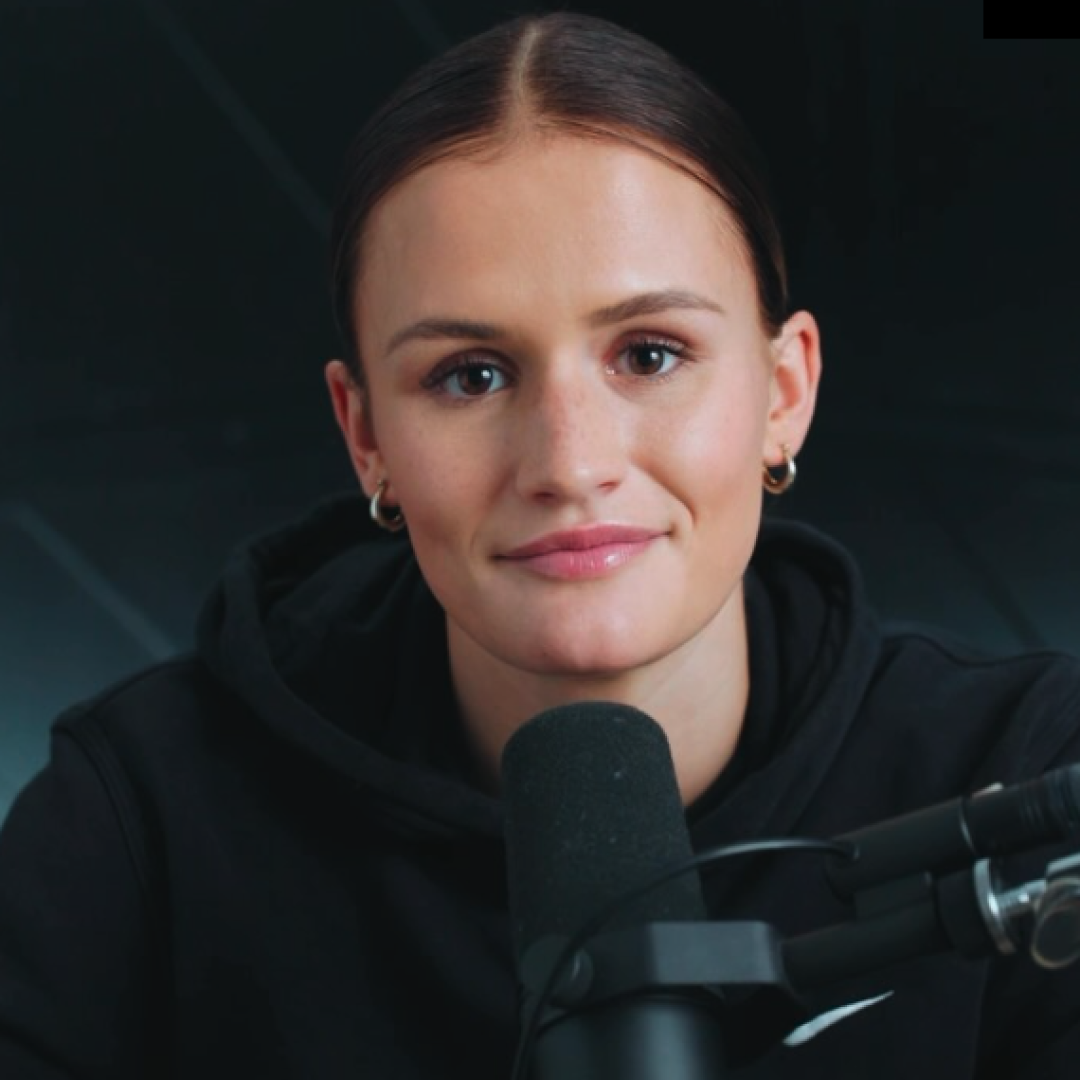 Person with a microphone, wearing a black hoodie, in a recording studio.