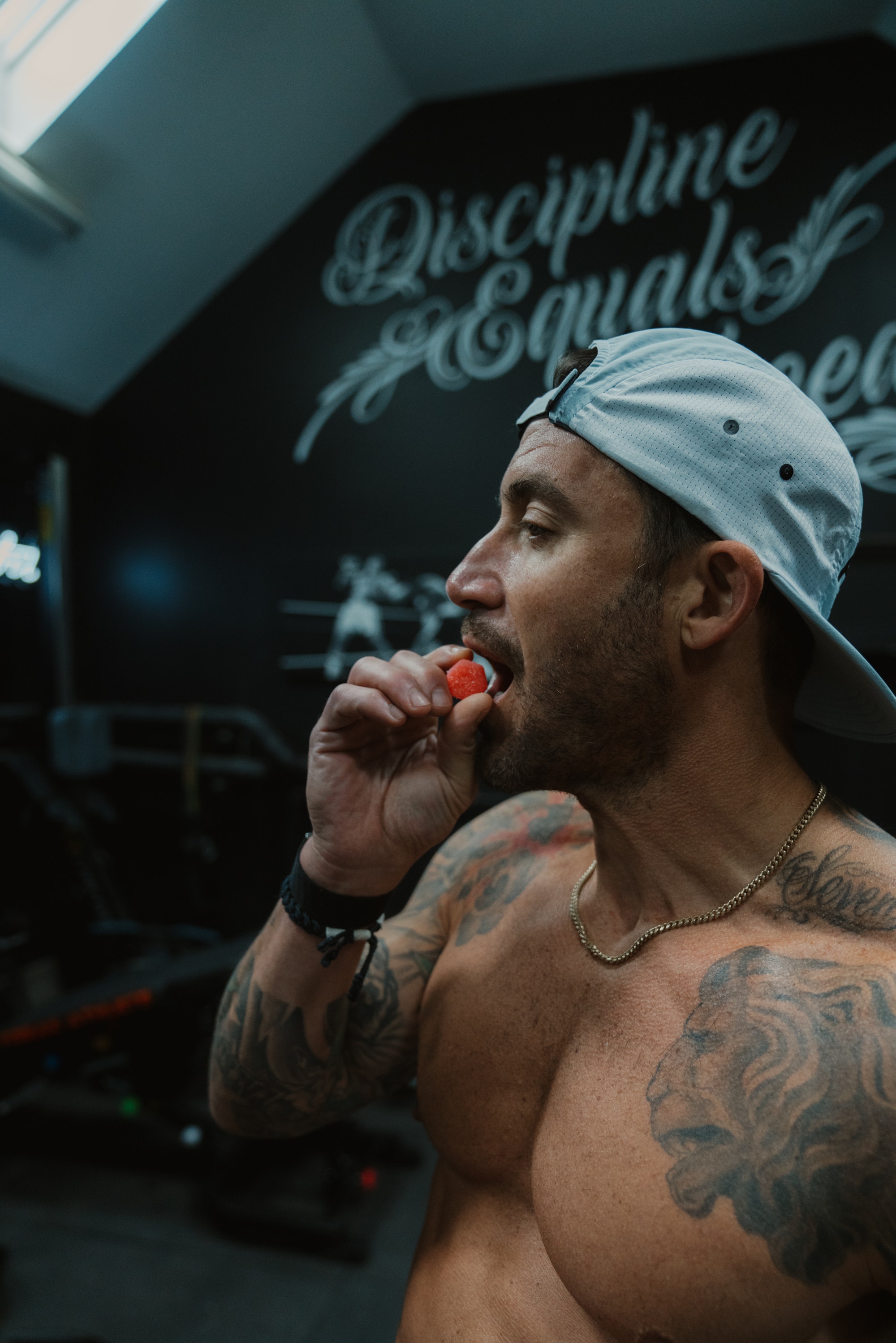 Man with tattoos eating a strawberry in a gym.