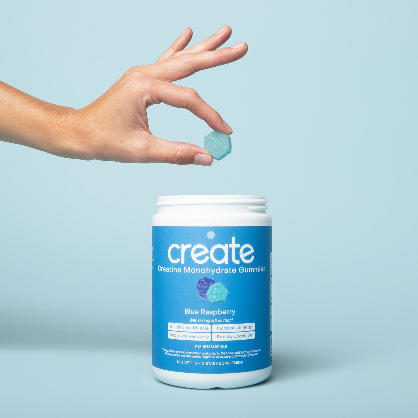 Hand holding a blue gummy over an open jar labeled 'create'.