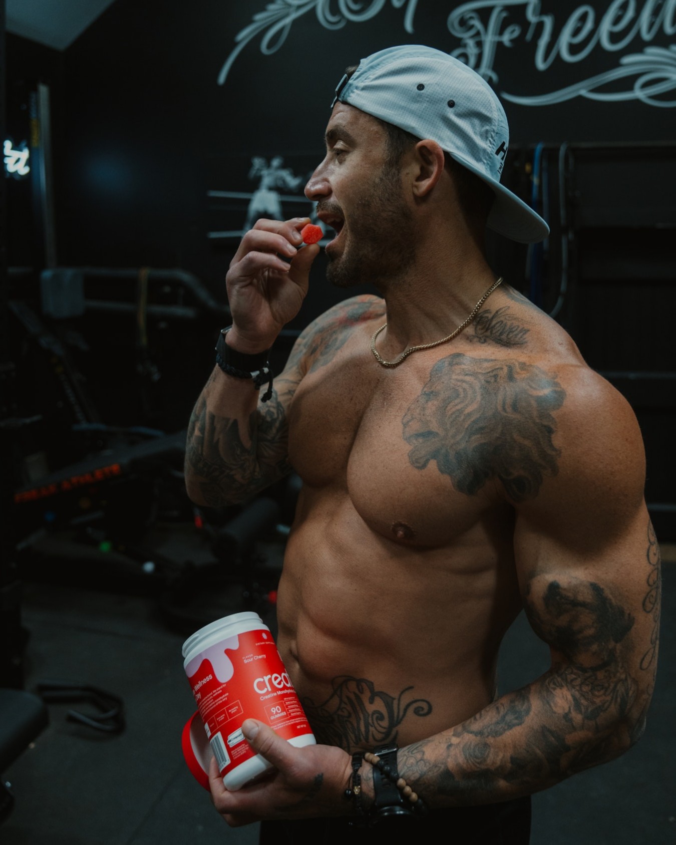 Tattooed man in gym eating supplement from a container.