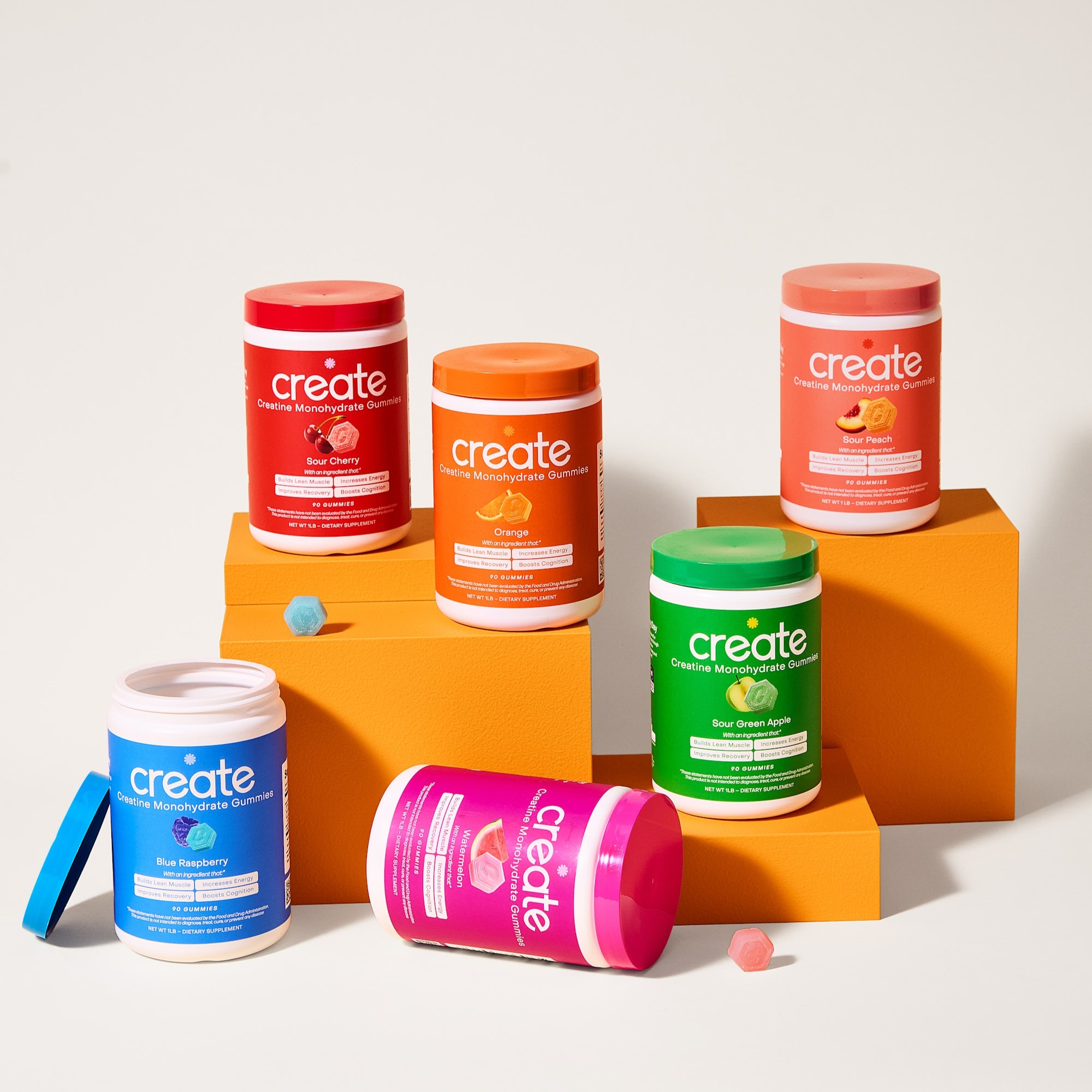 Colorful jars of creatine gummies on orange blocks.