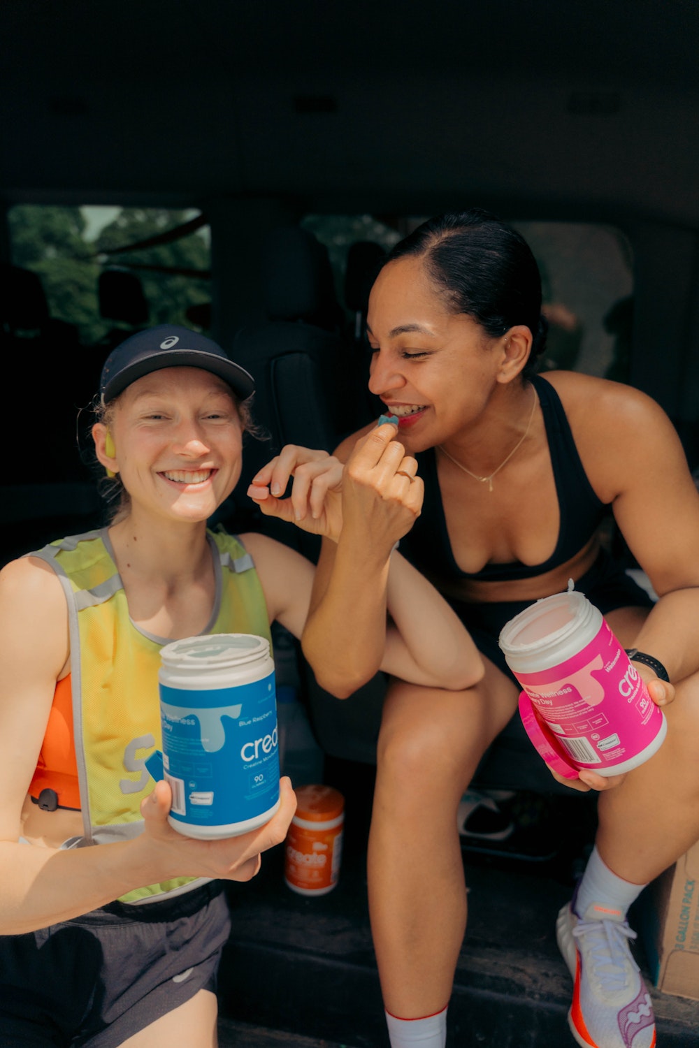 Two people sitting, holding containers of supplements, smiling and eating.