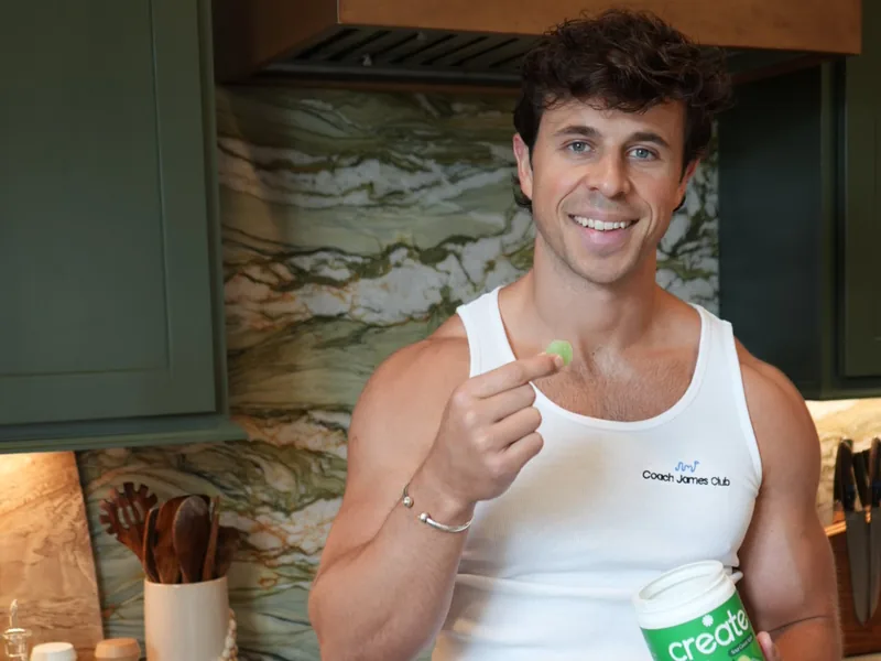A man in his kitchen smiling as he eats a Create gummy