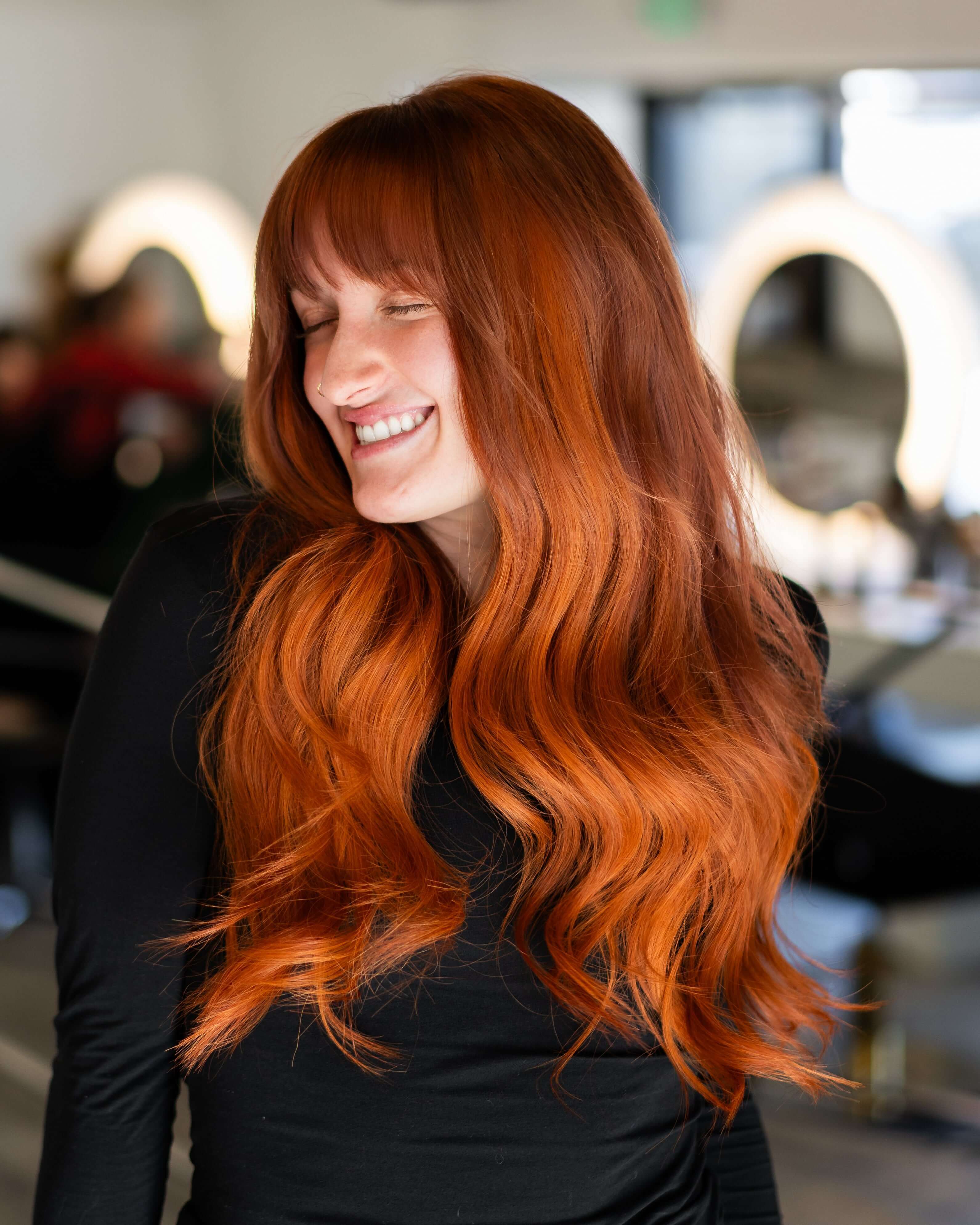 Smiling person with long, wavy red hair in a black top.
