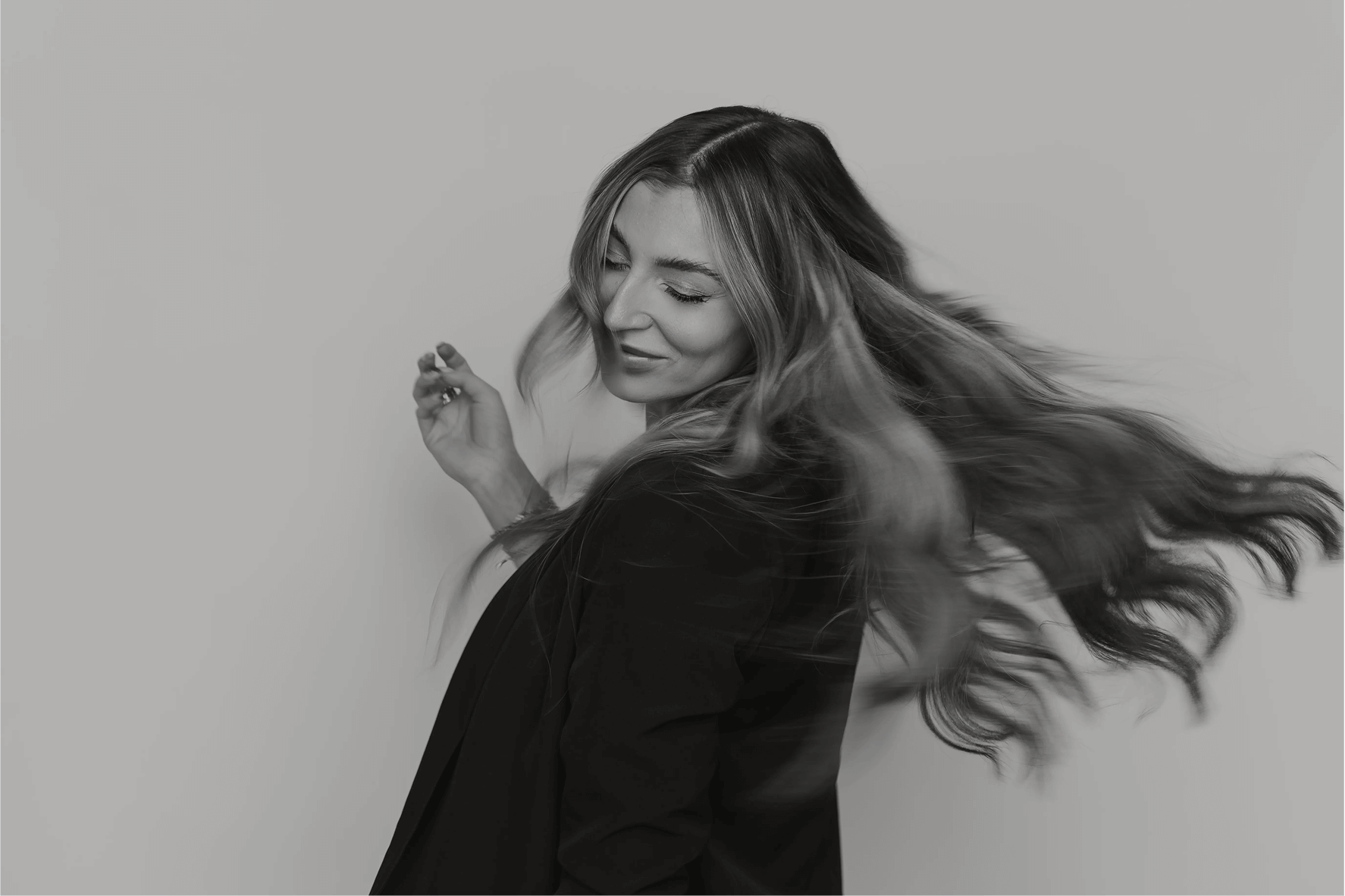 Smiling woman flipping her long, voluminous Bello Haven hair extensions, showing salon-quality shine and movement

