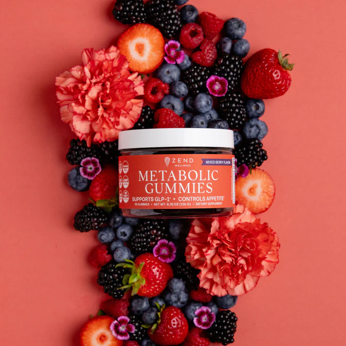 Jar of metabolic gummies surrounded by assorted berries and flowers on a red background.