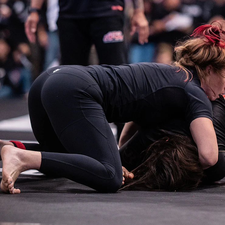 Two people in athletic wear grappling on a mat during a sports event.