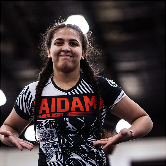 Person in a sports jersey with braided hair, smiling indoors.