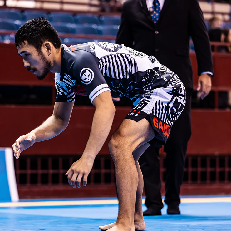 Man in grappling stance on a sports mat, wearing a black and white uniform.