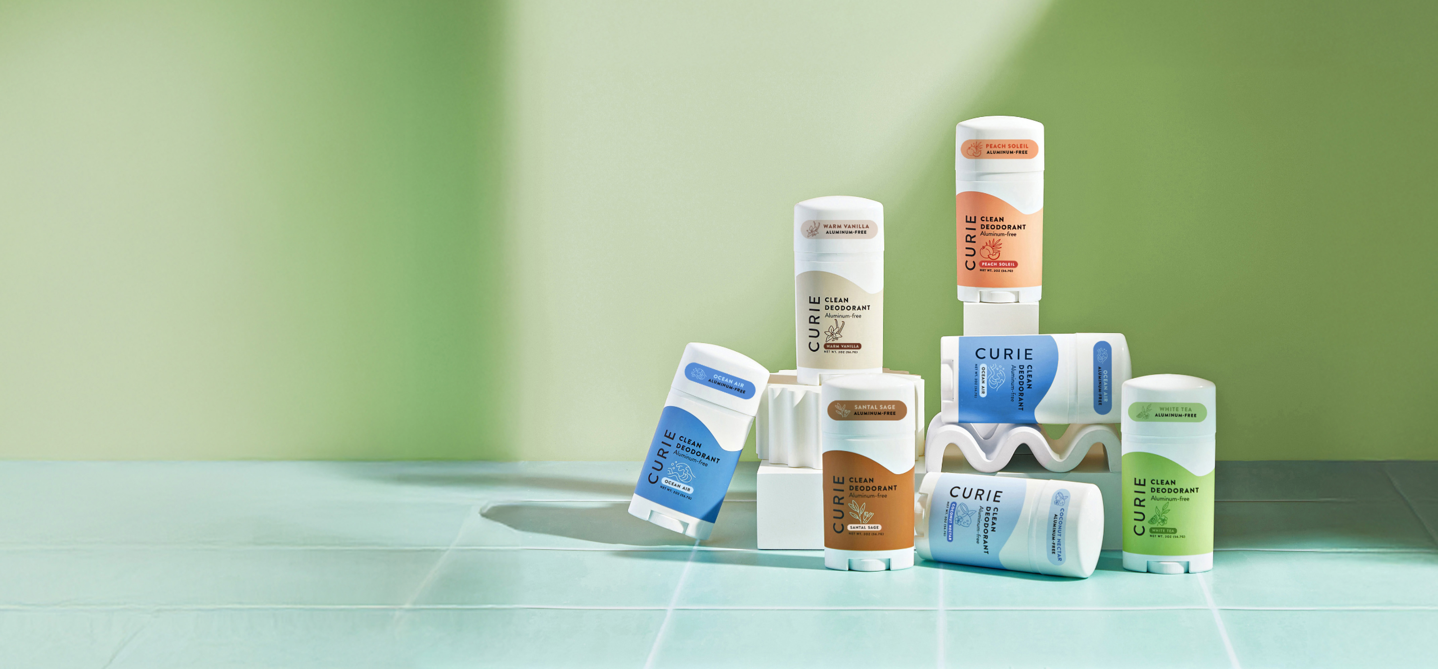 Assorted Curie deodorant sticks on a green and blue background.