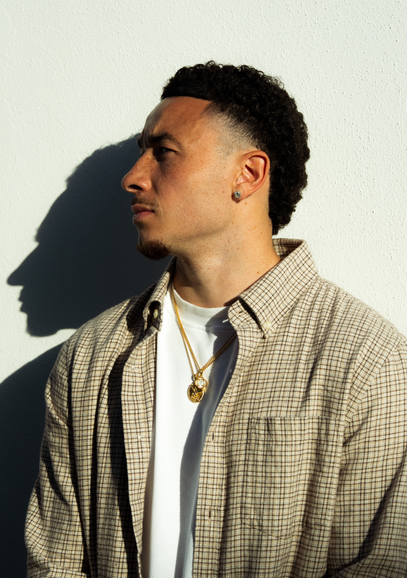 A man in profile stands against a white wall, with his shadow cast beside him.
