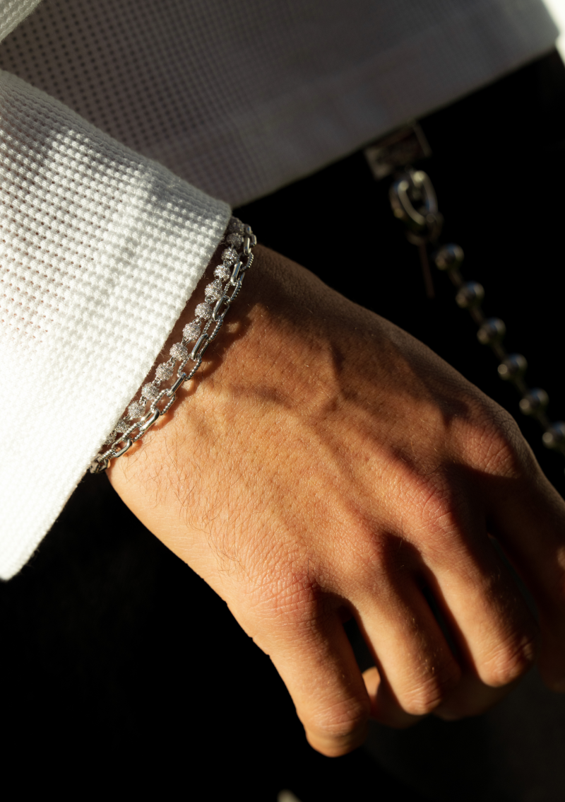 A close-up of a person's hand and wrist wearing a layered silver bracelet and a white shirt.