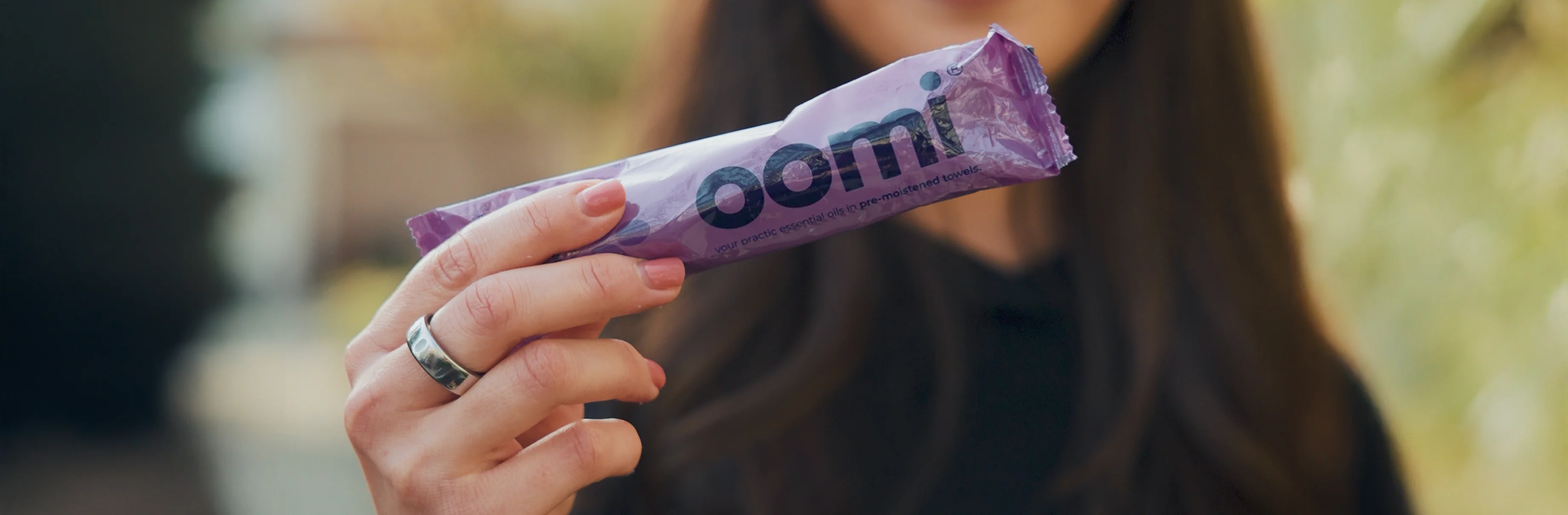 A close-up of a person's hand holding a purple product package labeled 'oomi'.
