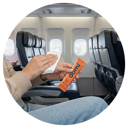 A person on an airplane holding a wipe and a small orange packet labeled 'oomi'.