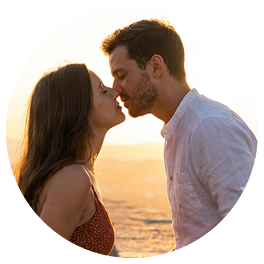 A man and woman framed in a circle, leaning in to kiss with a golden sunset in the background.