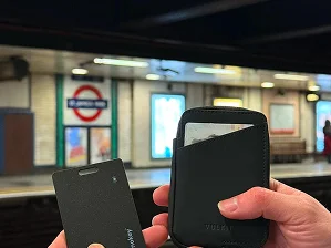 Hands holding a card and wallet at a subway platform.