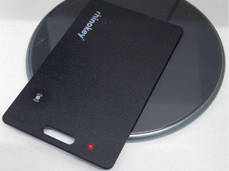 Black rectangular card with a small red light, placed on a round black surface.