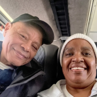A smiling man in a dark cap and a woman in a white beanie take a selfie on a bus.