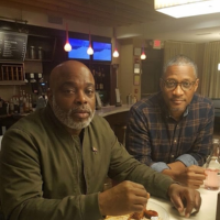 Two men sit at a restaurant counter, looking toward the camera.