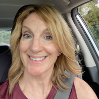 A smiling woman with blonde hair sits in the driver's seat of a car.