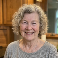 A headshot of a smiling older woman with short, wavy gray hair, wearing a striped shirt.