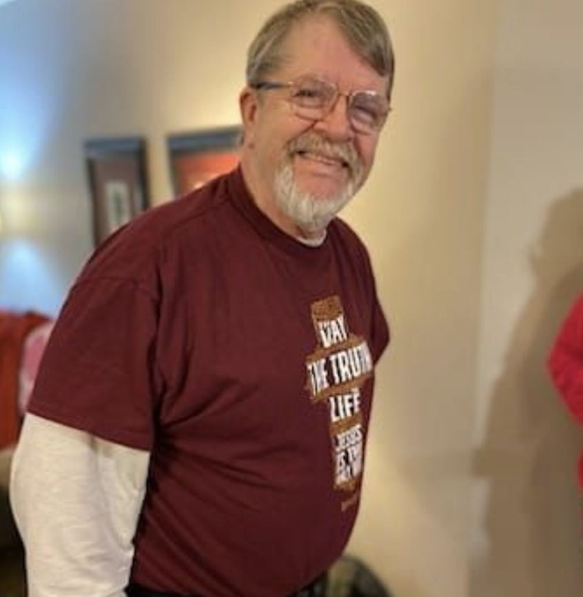 Smiling man in glasses wearing a maroon shirt indoors.