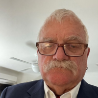 A close-up photo of an older man with a mustache and glasses, wearing a suit jacket.