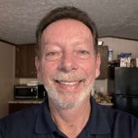 A headshot of a smiling, middle-aged man with a goatee, wearing a blue polo shirt.