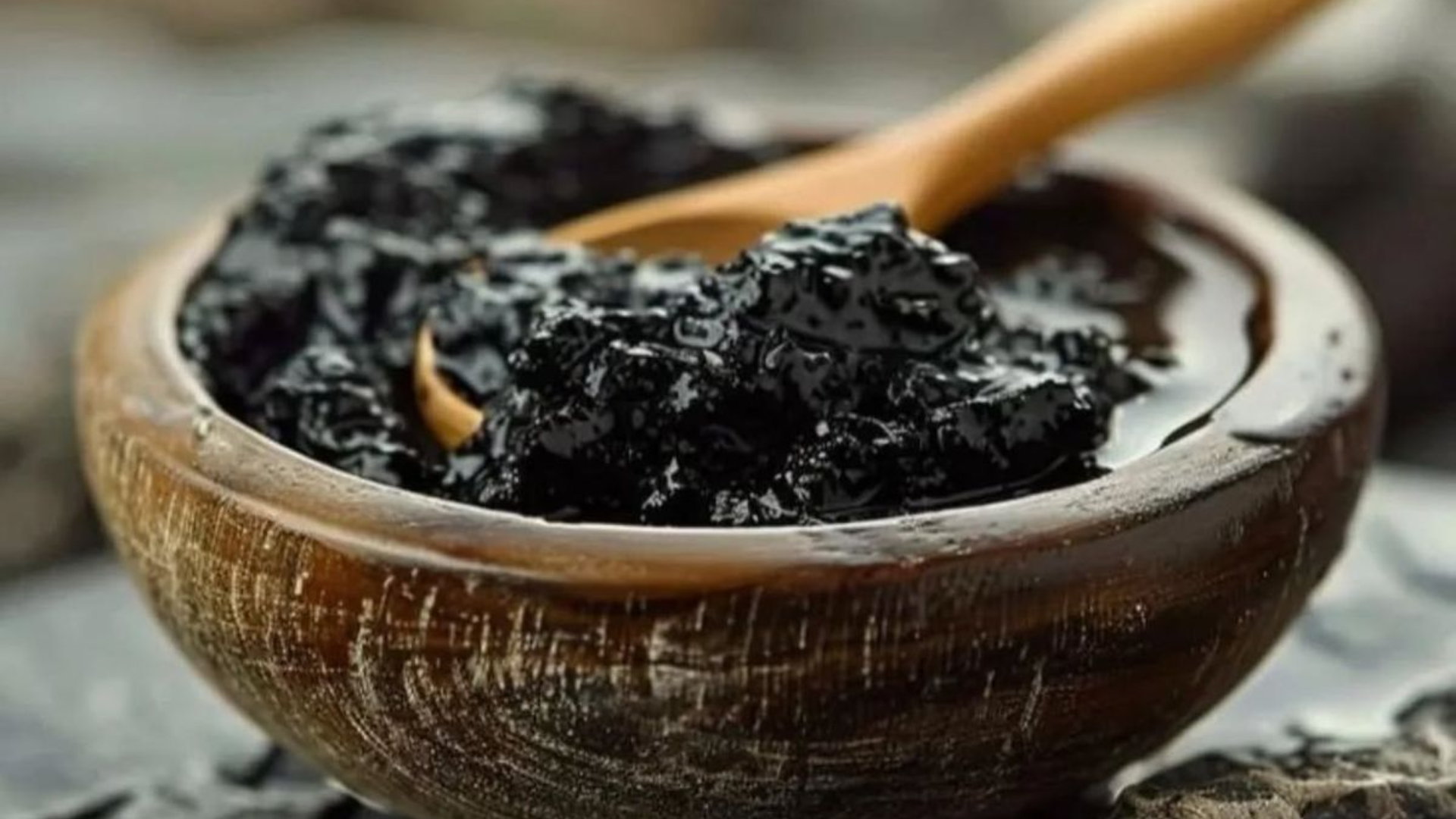 A close-up of a thick, black paste in a rustic wooden bowl with a wooden spoon.