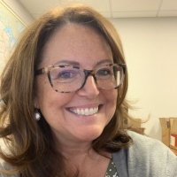 A headshot of a smiling woman with brown hair and tortoiseshell glasses.