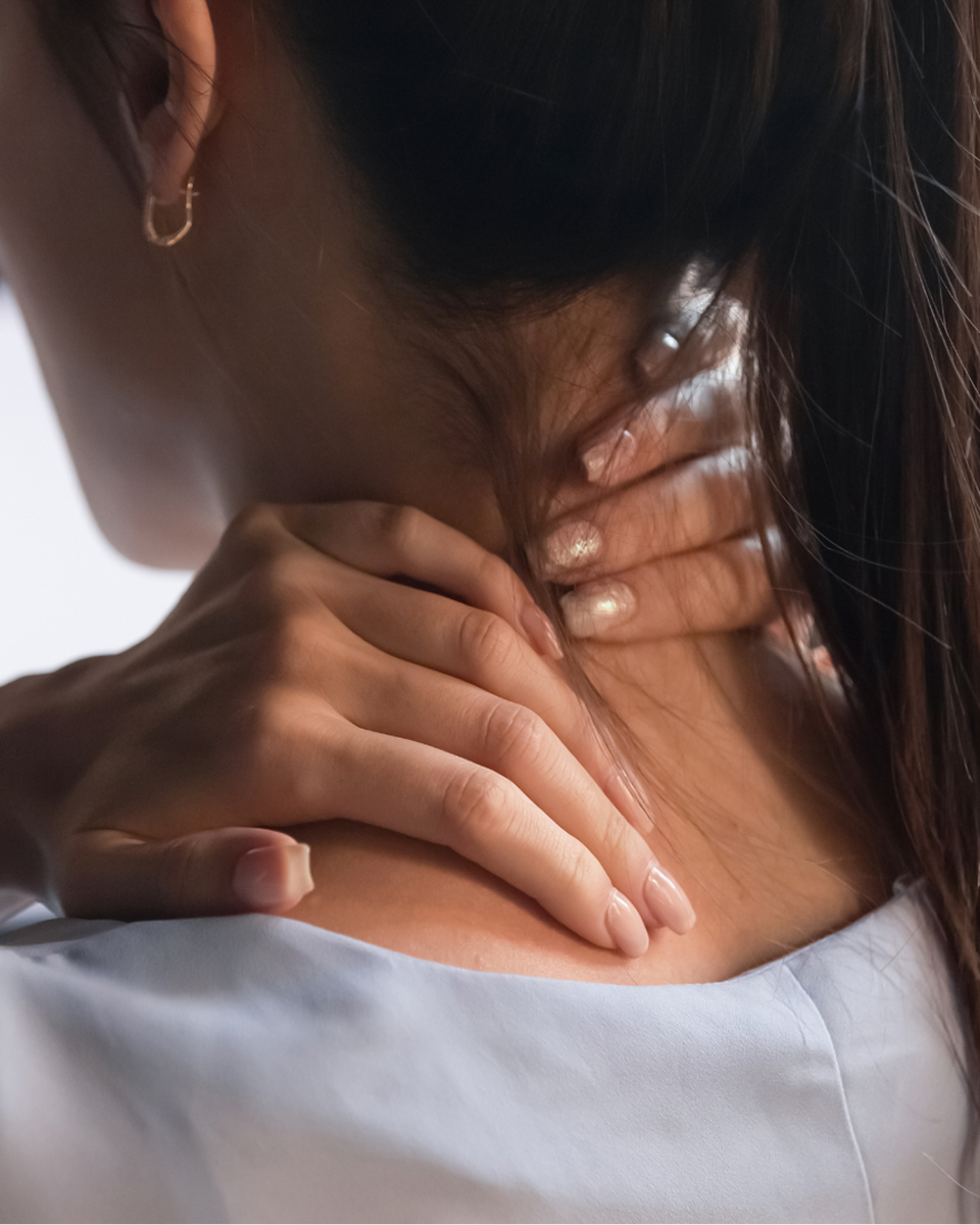 Person touching their neck with both hands, wearing a light blue shirt.