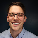 A person wearing glasses smiles against a dark background.