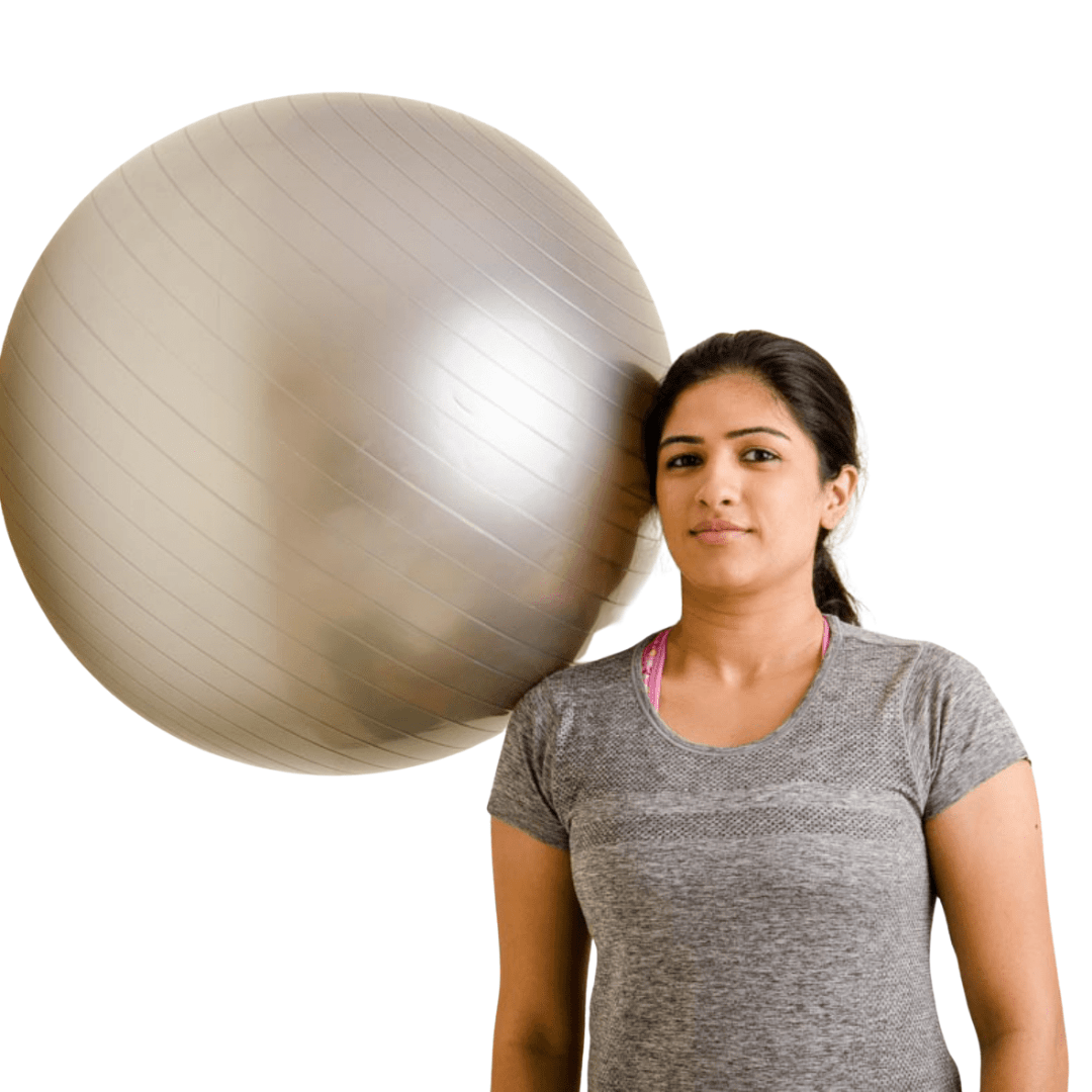 A woman standing with a large exercise ball beside her shoulder against a white background.