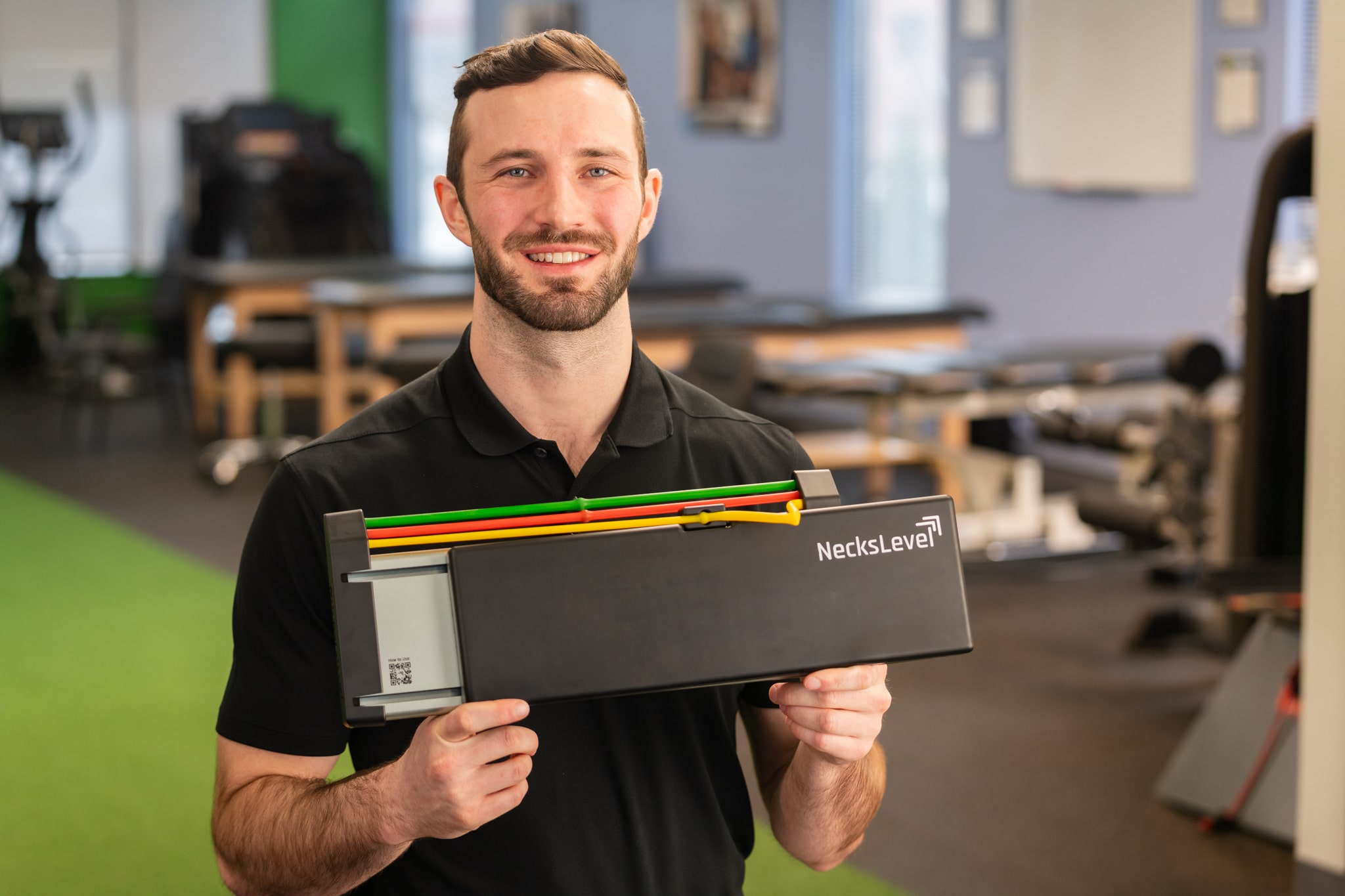 Man holding a NecksLevel exercise device in a gym setting.