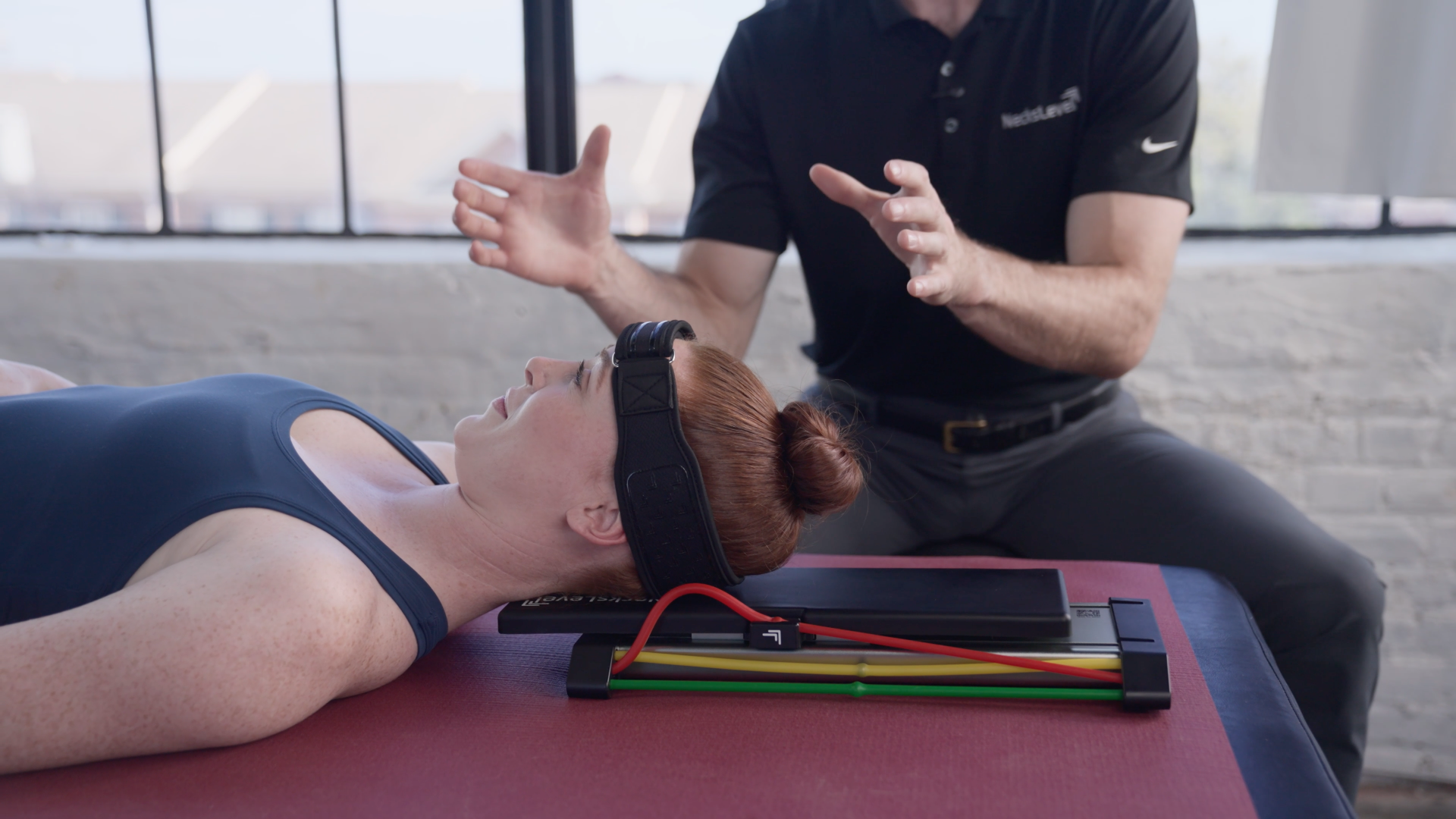 Person lying down with headgear, guided by another person gesturing.