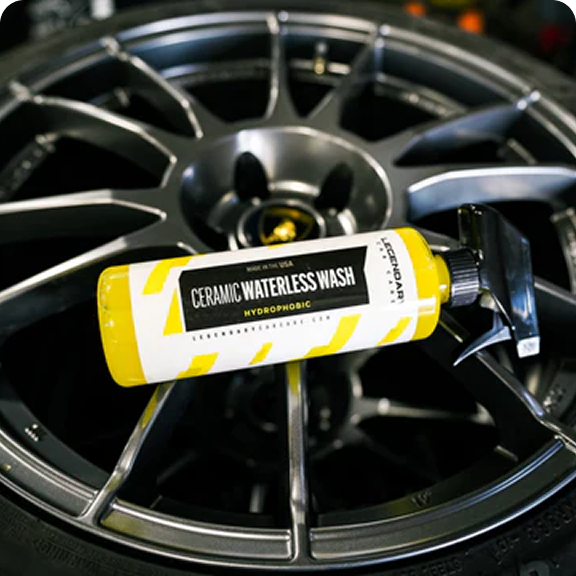 A bottle of Ceramic Waterless Wash car cleaner resting on the spokes of a dark grey wheel.