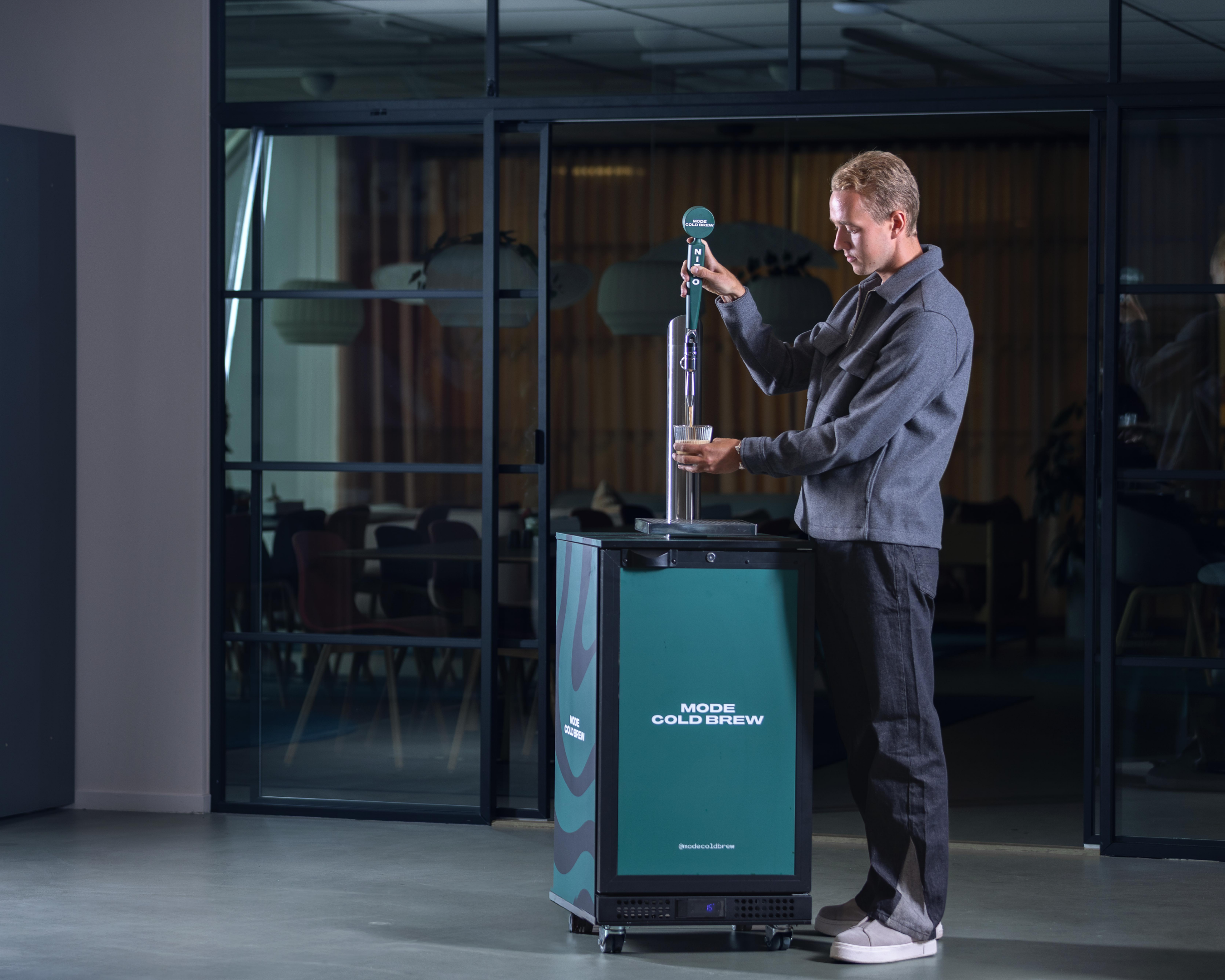 Person using a cold brew coffee dispenser in an office setting.