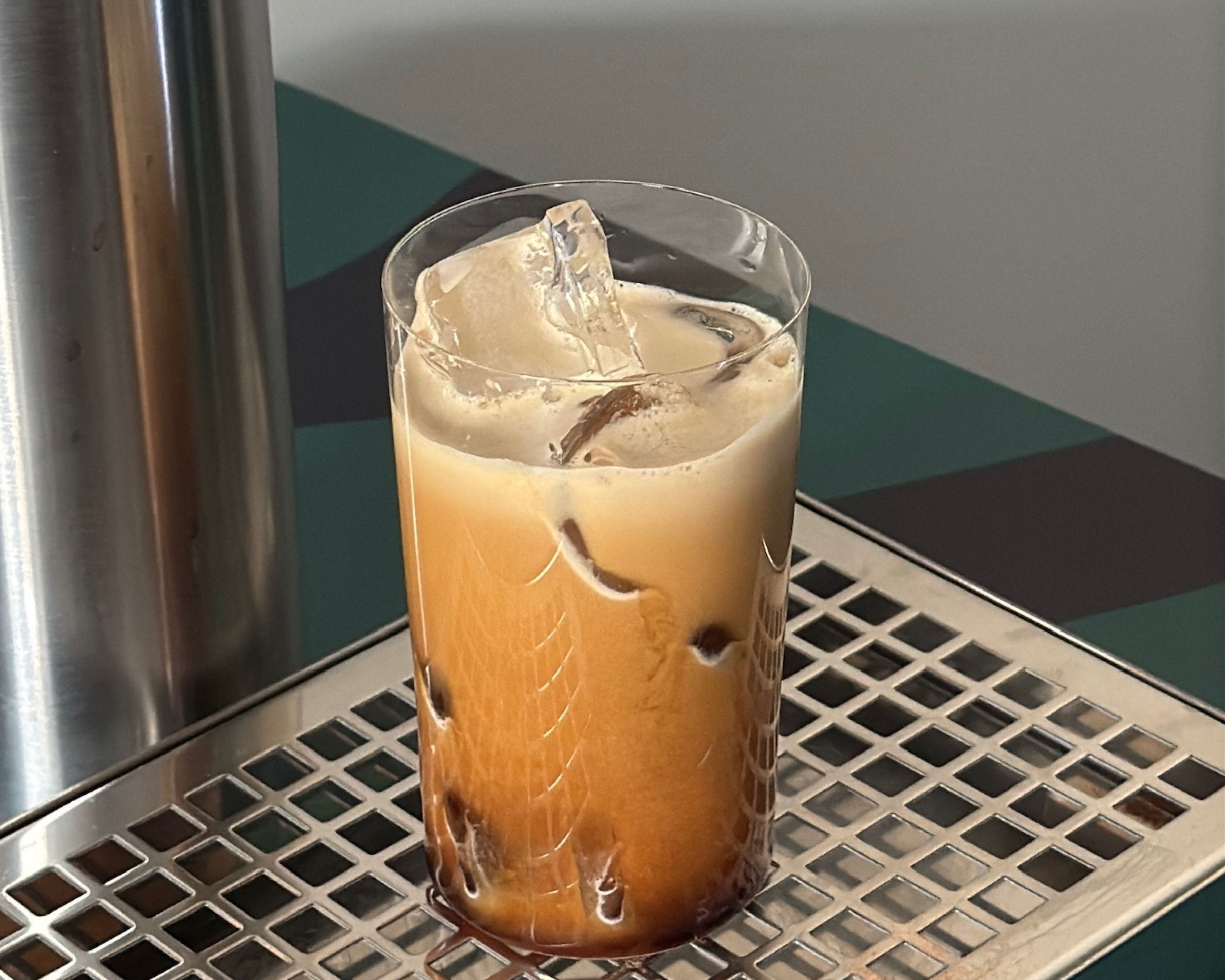 A glass of iced coffee with milk on a metal grid surface.