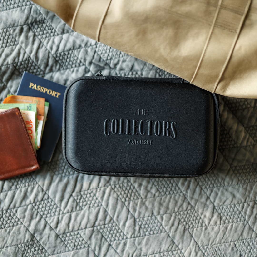 Black watch case, passport, wallet with bills on a quilted surface.