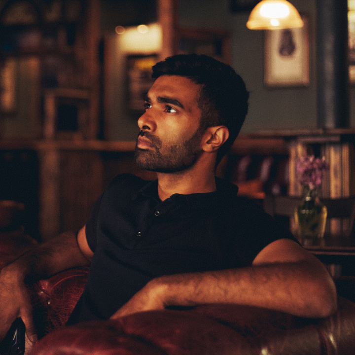 Man sitting on a leather couch in a dimly lit room.