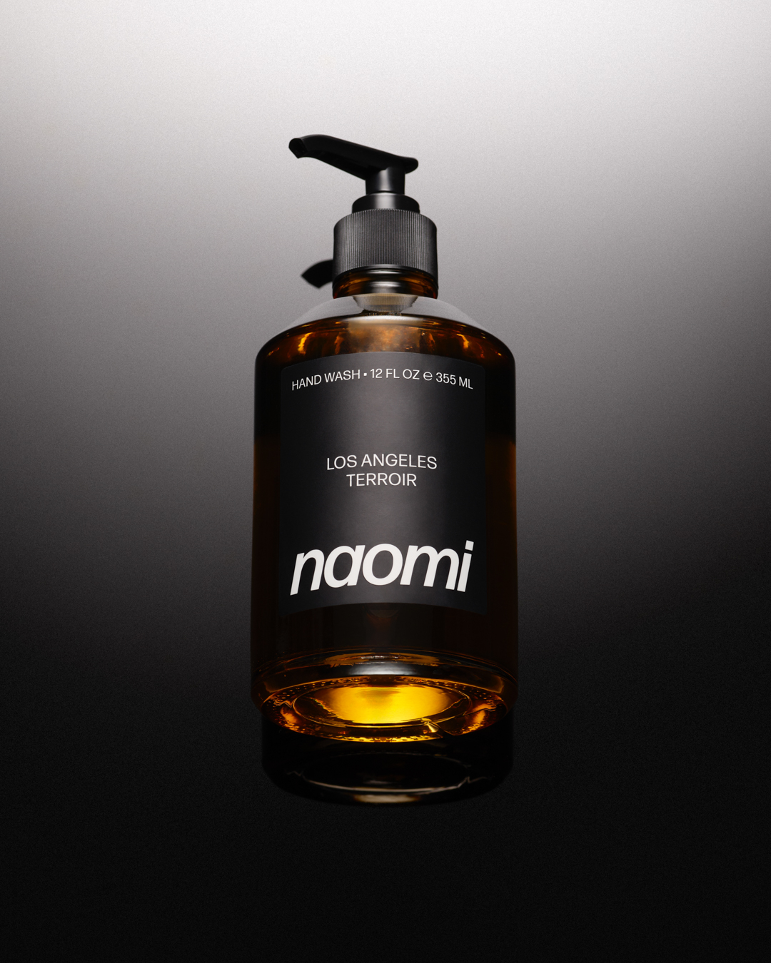 A brown glass pump bottle of Naomi Los Angeles Terroir hand wash against a dark, gradient background.