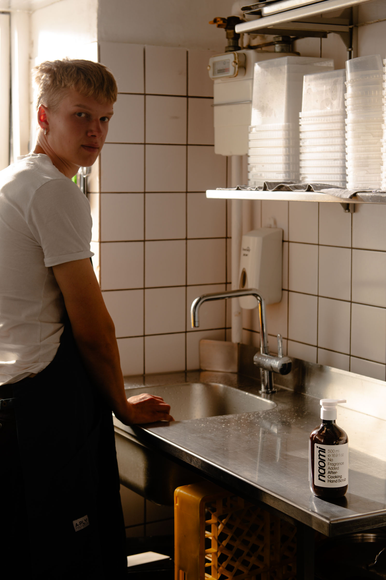 Person standing by a kitchen sink with a bottle of hand soap.