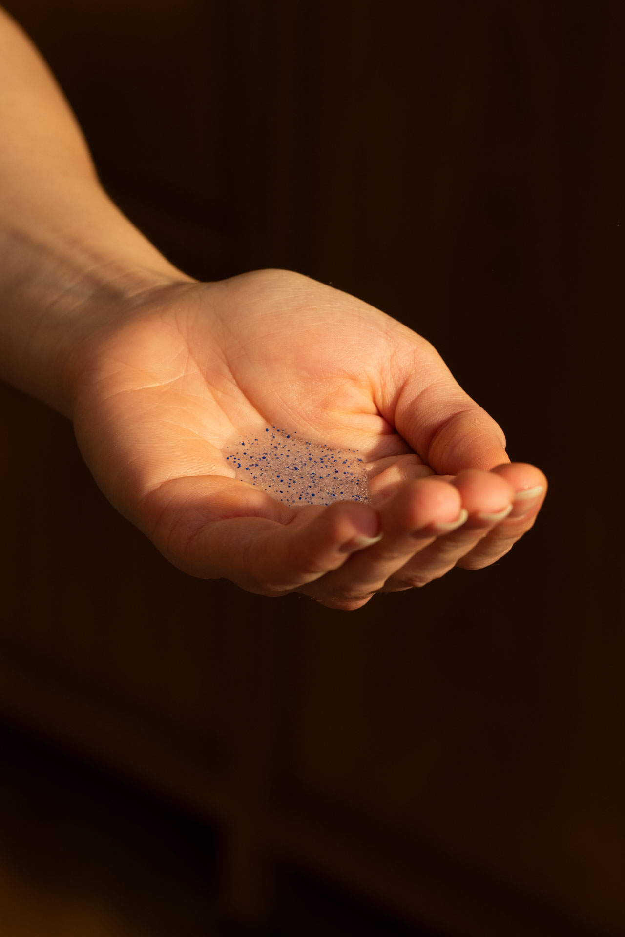 A hand holding a small amount of gel with blue specks.
