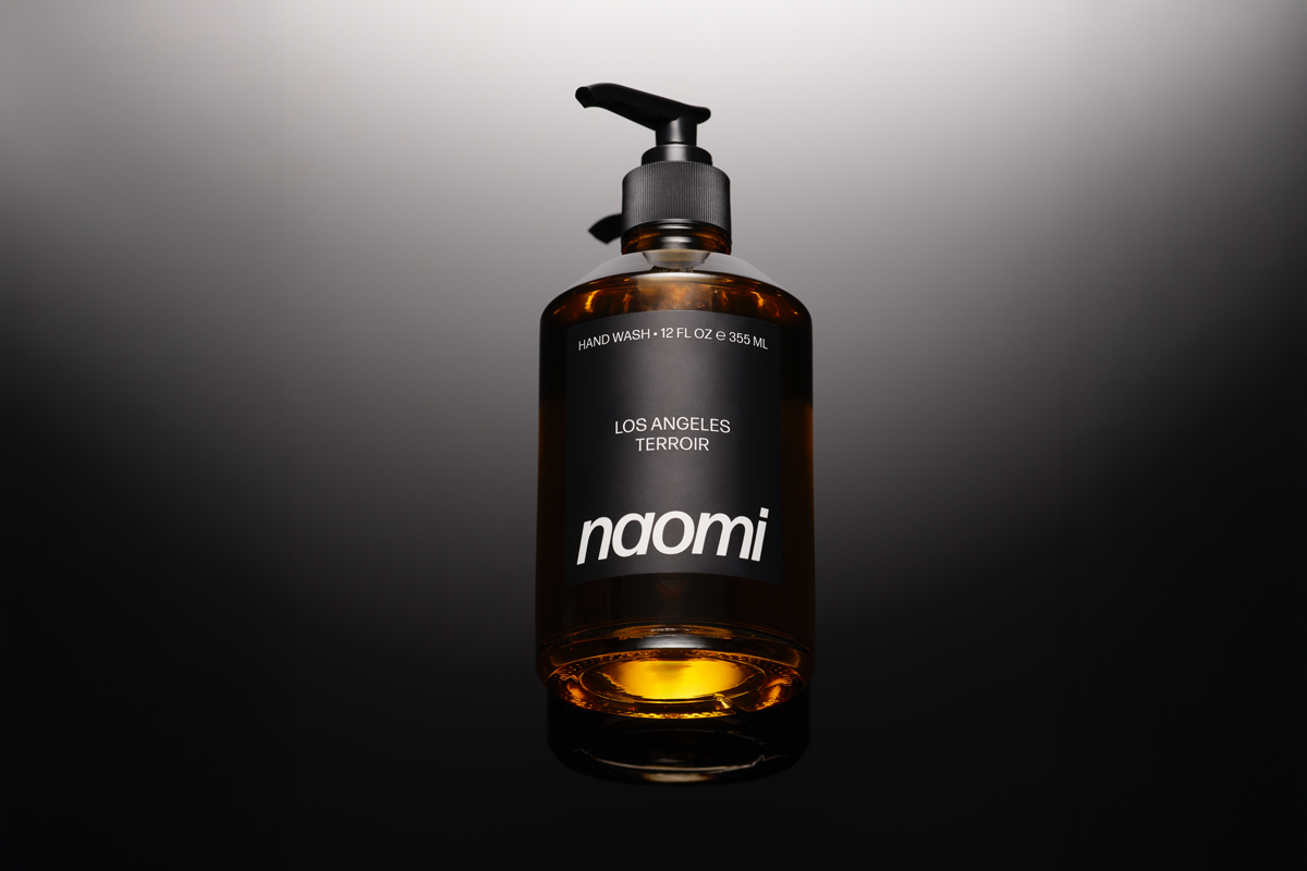 A brown glass pump bottle of Naomi brand hand wash on a dark, reflective surface.
