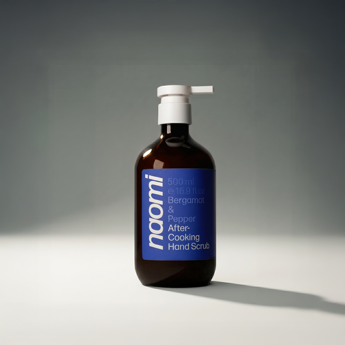 A brown pump bottle of Naomi After-Cooking Hand Scrub with a blue label against a grey background.