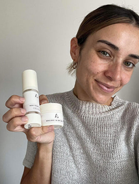A woman in pink athletic wear holds two white pouches in front of her face under a bridge.